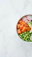 Fresh salmon poke bowl with edamame, avocado, radish, and cucumber on a white marble surface, top view.