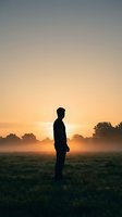 Silhouette of young man standing in misty field at golden sunrise with trees in background creating peaceful morning atmosphere for meditation concepts.