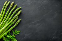 Fresh green asparagus spears and parsley leaves arranged on dark slate background with copy space. Food photography layout for menu or recipe.