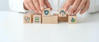 Hands arranging wooden blocks with healthcare and medical icons including stethoscope, shield, and green symbols on white background for wellness concepts.