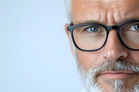 Close up portrait of mature Caucasian man with gray beard and modern black glasses looking confidently at camera against light blue background.
