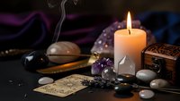 Mystical fortune telling setup with burning candle, tarot cards, crystals, incense and spiritual divination tools on dark atmospheric background.
