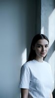 Young Caucasian woman in white t-shirt standing by concrete wall with natural window light shadows creating modern minimalist portrait for lifestyle branding.