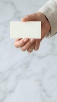 Male hand holding blank white business card against marble background, wearing light linen shirt sleeve. Isolated card ready for branding and design mockups.