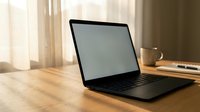 Modern laptop computer with blank screen on wooden desk in bright home office workspace with coffee cup and natural sunlight streaming through window.
