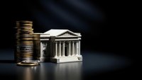 Golden coins stacked beside classical bank building model on dark surface with dramatic lighting for financial investment concepts.