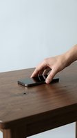 Close-up of a Caucasian male hand reaching for a smartphone on a wooden table surface. Suitable for technology, communication, and mobile device concepts.