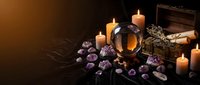 Mystical fortune telling setup with crystal ball, amethyst gems, burning candles and ancient books on dark wooden table for divination and spiritual practices.