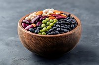 Colorful variety of raw legumes and beans in wooden bowl on dark background, including black, red kidney, mung and white beans for healthy cooking.