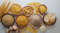Various raw pasta types, grains and flour in wooden bowls arranged on light background. Ingredients for Mediterranean cuisine and healthy cooking.