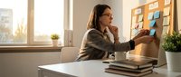 Professional businesswoman organizing colorful sticky notes on office wall during strategic planning session in modern workplace.