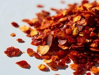 Crushed red pepper flakes scattered on white background, dried chili spice seasoning for cooking and culinary applications.