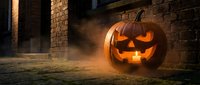 Glowing jack-o-lantern with carved face sits on ground near brick wall with fog and dramatic orange lighting for seasonal decorations.