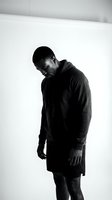 Man with dark skin tone wearing black hoodie and shorts standing with head bowed in contemplative pose against white background for portrait, mental health, wellness, and lifestyle concepts.