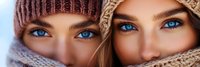 Two young Caucasian women with striking blue eyes wearing cozy knit winter hats and scarves, close-up portrait showing friendship and warmth during cold season.