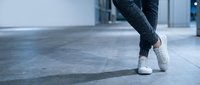 Person in jeans and white sneakers walking on modern tiled floor in contemporary urban interior space for lifestyle and fashion concepts.