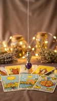 Mystical tarot card reading setup with ornate pendulum, warm fairy lights and dried lavender creating atmospheric fortune telling scene for spiritual guidance.