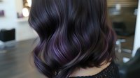 Dark wavy hair with purple balayage highlights styled in loose curls, showing modern hair coloring technique and professional salon result.