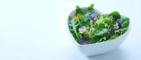 Fresh mixed green salad with purple flowers and edible blossoms in white bowl on light background, suitable for healthy eating, nutrition, and food photography.