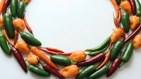 Fresh chili peppers arranged in circular frame on white background. Green, orange and red hot peppers for cooking, spice and food design projects.