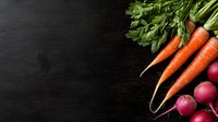 Fresh organic carrots with green tops and vibrant red radishes arranged on dark black slate background, copy space for menu or recipe design.
