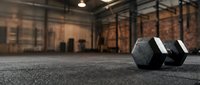 Pair of black hexagonal dumbbells on rubber gym floor in industrial loft fitness studio with exposed brick walls and metal framework for strength training and workout design.