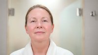 Professional middle-aged Caucasian female doctor in white medical coat smiling confidently in modern hospital corridor for healthcare marketing.