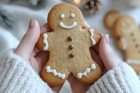 Freshly baked gingerbread cookie with white icing decoration and smiling face held in hands wearing cozy knit sweater against soft winter holiday background.