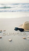 Summer written in sand on a sunny beach with straw hat, sunglasses, and seashells, ocean waves in background.