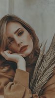 Young Caucasian woman with blonde wavy hair in beige sweater holding pampas grass against concrete wall background for autumn fashion and lifestyle content.