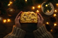 Hands holding homemade fruitcake surrounded by Christmas decorations and warm lights creating festive holiday baking atmosphere for seasonal celebrations.