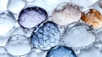 Water droplets with soap bubbles in soft blue and brown tones create abstract macro photography pattern showing surface tension and light refraction.