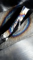 Abstract metallic surface with rainbow light refraction creating prismatic spectrum colors through scratched industrial texture for modern design backgrounds.