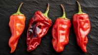 Fresh red chili peppers arranged in row on black slate background, one dried pepper among fresh ones showing food preservation process.