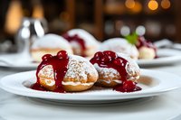 Freshly baked profiteroles with powdered sugar and cherry sauce served on white plates in restaurant setting with soft bokeh background.