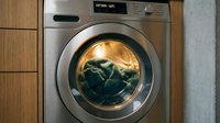 Modern silver washing machine with open door showing dark clothes inside, built into wooden cabinetry in contemporary laundry room interior.