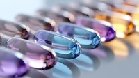 Colorful pharmaceutical capsules in row showing gradient from blue to purple and orange, macro photography with selective focus and reflection.