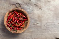 Dried red chili peppers in wooden bowl on rustic table. Spicy cooking ingredients for hot sauce, seasoning and culinary preparations.
