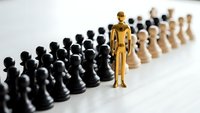 Golden wooden figure standing out among black and white chess pieces representing leadership, uniqueness and strategic thinking in business concepts.