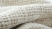 Soft knitted fabric in cream color with textured pattern close-up. Natural wool or cotton material showing detailed stitch structure in warm neutral tones.