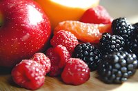 Fresh mixed berries and fruits macro shot showing vibrant red raspberries, dark blackberries, and red apple on wooden surface. Natural food photography for healthy eating.