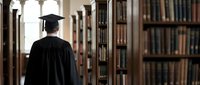 Graduate student in cap and gown walking through historic university library with wooden bookshelves for academic achievement and education concepts.