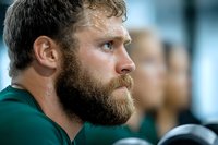 Caucasian male athlete with thick beard and intense expression wearing green jersey, photographed in profile against blurred background during sports event.