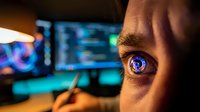 Futuristic cyberpunk eye with digital holographic interface reflection in iris showing data streams and code on computer screens in dark tech environment.