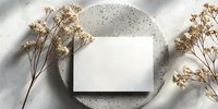 Blank white card on concrete plate with dried flowers creating minimalist composition for wedding invitation, business branding, or elegant announcement.