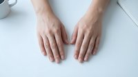 Female hands with natural manicure placed flat on white surface showing clean fingernails and smooth skin texture for beauty and skincare concepts.