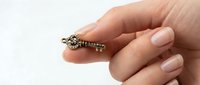Hand holding vintage brass ornate key between fingers on white background for security and access concepts.
