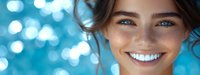 Young woman with bright blue eyes and radiant smile against blurred blue background with bokeh effect, conveying happiness and confidence.