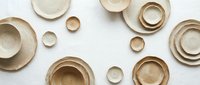 Elegant beige ceramic dinnerware set with plates and bowls in various sizes arranged on white background for modern kitchen and dining decor.