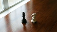 Black and white chess pieces king and knight on wooden floor near window with natural light for strategic thinking and competition concepts.